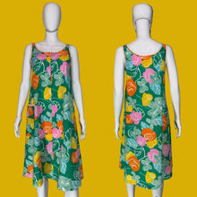Load image into Gallery viewer, A sleeveless A-line dress displayed on two white mannequins against a black background, showing front and back views. The dress features a vibrant green base with a retro floral pattern in pink, orange, yellow, and white.