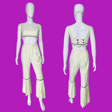Load image into Gallery viewer, A cream-colored two-piece outfit displayed on a white mannequin, showing both front and back views. The set includes a sleeveless crop top with black dashed trim and matching high-waisted flared pants with black dashed trim and decorative buttons on the back.