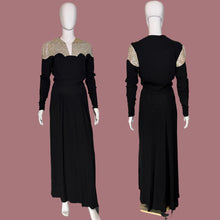 Load image into Gallery viewer, A long black dress displayed on a white mannequin from the front and back. The dress features a V-neckline with beige and gold patterned lace-like shoulder panels and long sleeves.