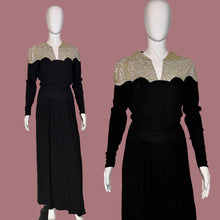 Load image into Gallery viewer, A long black dress displayed on a white mannequin shown in a wide shot and a close up. The dress features a V-neckline with beige and gold patterned lace-like shoulder panels and long sleeves.