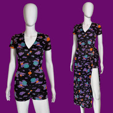 Load image into Gallery viewer, A women's short-sleeve romper and matching wrap skirt set displayed on white mannequins against a plain indoor wall. The set features a black base with a colorful abstract cloud-like print in purple, teal, orange, and pink.
