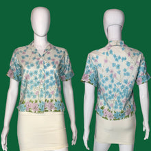 Load image into Gallery viewer, A short-sleeve button-front blouse with a floral print, shown on a white mannequin from both the front and back views. The blouse features a white base with blue, pink, and green floral motifs.
