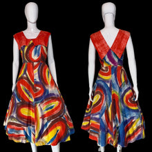 Load image into Gallery viewer, A sleeveless A-line dress displayed on a white mannequin, shown from both front and back views. The dress features a bold abstract swirl pattern in red, blue, yellow, and white, with a solid red V-neckline on the back and dramatic collar.