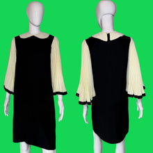 Load image into Gallery viewer, A black dress with dramatic white sleeves displayed on a white mannequin, shown from both front and back view. The dress features a round cream collar and long cream pleated bell sleeves with black trim at the cuffs.
