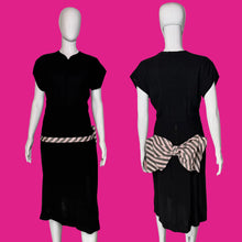 Load image into Gallery viewer, A black short-sleeve dress shown on a white mannequin from both front and back views, featuring a pink and white striped waist sash with a large bow at the back waist.
