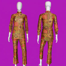 Load image into Gallery viewer, A two-piece matching set consisting of a long-sleeve mock-neck top and matching cropped pants, displayed on a white mannequin. The set features a vibrant, busy patchwork-style geometric print with orange, yellow, red, and black colors.