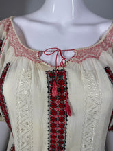 Load image into Gallery viewer, Close-up of a white garment with red and black embroidery on a mannequin.