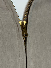 Load image into Gallery viewer, Close-up of a vintage-style brass zipper pull on a beige textured fabric garment.