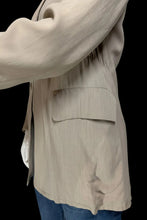 Load image into Gallery viewer, Close-up of a beige jacket with a side pocket, worn over blue jeans against a plain white background.