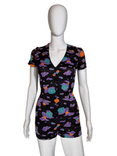 Load image into Gallery viewer, A short-sleeve romper displayed on a white mannequin against a plain light gray wall. The romper has a black base with a colorful cloud-like pattern in purple, teal, and orange.
