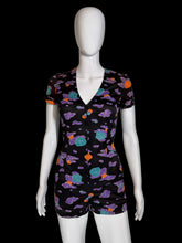 Load image into Gallery viewer, A short-sleeve romper displayed on a white mannequin against a plain light gray wall. The romper has a black base with a colorful cloud-like pattern in purple, teal, and orange.
