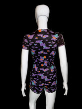 Load image into Gallery viewer, A short-sleeve romper displayed on a white mannequin from the back, featuring a black base with a colorful abstract cloud-like pattern in purple, teal, and orange.