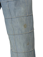Load image into Gallery viewer, A close-up of a light blue denim fabric item, showing stitched panel seams and a few small stains.