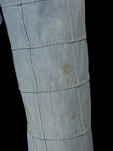 Load image into Gallery viewer, A close-up of a light blue denim fabric item, showing stitched panel seams and a few small stains.