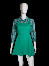 Load image into Gallery viewer, A vintage green pinafore dress displayed on a white mannequin. The dress features a solid green body with a printed collar and shoulder straps, accented by three decorative buttons.
