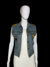 Load image into Gallery viewer, A light blue denim vest displayed on a white mannequin. The vest has yellow patches on the shoulders, a yellow circular patch on the chest, and a small red-and-white rectangular patch near the lower right side.