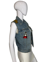 Load image into Gallery viewer, A light blue denim vest displayed on a white mannequin. The vest has yellow embroidered shoulder patches, a front snap closure, flap pockets, and a small red-and-black patch on the chest.