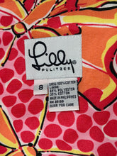 Load image into Gallery viewer, Close-up of a colorful garment label sewn onto a patterned fabric. The fabric has a bold abstract print in orange, red, pink, yellow, and black.