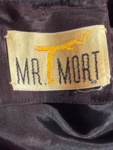Load image into Gallery viewer, Close-up of a beige fabric brand label sewn onto dark satin-like clothing, with the embroidered text 'MR. MORT' in black and a yellow figure.
