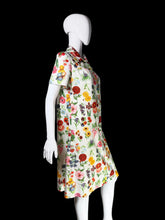 Load image into Gallery viewer, A white short-sleeve dress with a dense multicolor floral print, displayed on a white mannequin against a plain white wall.