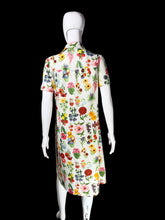 Load image into Gallery viewer, A short-sleeve collared dress displayed on a white mannequin, showing a colorful all-over floral print on a white base. The dress features a variety of flowers in pink, red, yellow, orange, and green, photographed against a plain white wall.