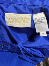 Load image into Gallery viewer, Close-up of the inside neck area of a bright royal blue garment, showing a cream embroidered Cache brand label and a white material tag with size 2 and fabric composition details.