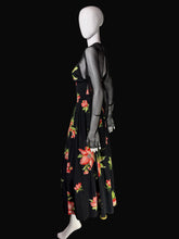 Load image into Gallery viewer, A black maxi dress with a vibrant red and pink floral print and sheer black mesh sleeves, displayed on a white mannequin in front of a black background.