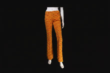 Load image into Gallery viewer, Orange and yellow patterned flared pants displayed on a white mannequin with a black background.