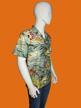 Load image into Gallery viewer, A men's short-sleeve button-up shirt with a colorful tropical and scenic print, displayed on a white mannequin wearing blue jeans against a black background.