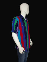 Load image into Gallery viewer, A mannequin wearing a short-sleeve collared button-up shirt with bold horizontal stripes in red, blue, green, purple, and navy, paired with dark jeans against a black background.