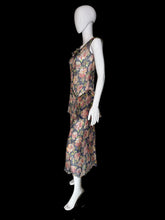 Load image into Gallery viewer, A sleeveless dress with a floral print. The dress features a navy blue base with pink, red, and green floral patterns, and a ruffled asymmetrical hem.