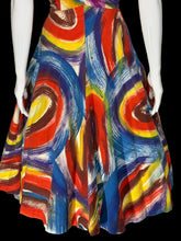 Load image into Gallery viewer, A close up of the skirt of a sleeveless A-line dress displayed on a white mannequin. The dress features a bold abstract swirl pattern in red, blue, yellow, and white.