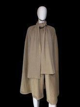 Load image into Gallery viewer, A beige ribbed knit cape with a draped collar and layered hem, displayed on a white mannequin.