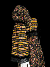 Load image into Gallery viewer, A close up of the sleeve of a maxi dress displayed on a white mannequin featuring a black base with yellow and orange horizontal stripes on the bodice and hem, and a central floral print panel in yellow, orange, and pink tones.