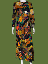 Load image into Gallery viewer, A long-sleeve maxi dress with a vibrant, dense floral and paisley print on a black base, displayed on a white mannequin.