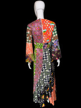 Load image into Gallery viewer, The back view of a long-sleeved patchwork maxi dress displayed on a mannequin. The dress features a vibrant multicolor patchwork design with various patterns including houndstooth, polka dots, florals, and plaid in orange, green, pink, black, white, and purple.