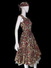 Load image into Gallery viewer, A sleeveless fit-and-flare dress with a matching headscarf displayed on a white mannequin. The dress features a vintage floral pattern in muted red, brown, and olive green tones over a cream base.