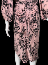 Load image into Gallery viewer, A pink midi dress with a black floral and botanical print, styled on a white mannequin. The dress features a gathered waist with a front tie knot, long puff sleeves, and a button-up front.