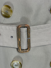 Load image into Gallery viewer, Close-up of a beige trench coat with a matching belt and a rusted metal buckle, featuring decorative buttons.