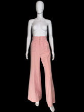Load image into Gallery viewer, A pair of high-waisted, wide-leg pink pants displayed on a white mannequin. The pants feature a buttoned waistband with gold-tone buttons and two large patch pockets in the front.