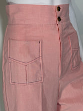 Load image into Gallery viewer, A close-up of a pair of pink high-waisted trousers displayed on a white mannequin. The back view shows a double button closure at the waistband, and a large decorative front patch pocket with contrast stitching.