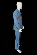 Load image into Gallery viewer, A side view of a blue denim two-piece set consisting of a long-sleeve button-front shirt and matching pants, displayed on a white mannequin. The shirt features colorful embroidered patterns on the chest in red, orange, and yellow.