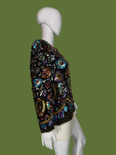 Load image into Gallery viewer, A long-sleeve embellished jacket displayed on a white mannequin. The jacket is heavily decorated with iridescent sequins and beads in black, gold, pink, blue, and green tones, featuring a central gold circular motif.