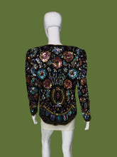 Load image into Gallery viewer, A long-sleeve embellished jacket displayed on a white mannequin. The jacket is heavily decorated with iridescent sequins and beads in black, gold, pink, blue, and green tones, featuring a central gold circular motif.