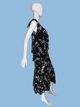 Load image into Gallery viewer, A black sleeveless dress with a colorful floral print, displayed on a white mannequin. The dress features a V-neckline, ruffled shoulder straps, and a tiered ruffle detail at the waist.