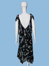 Load image into Gallery viewer, A black sleeveless dress with a colorful floral print, displayed on a white mannequin. The dress features a V-neckline, ruffled shoulder straps, and a tiered ruffle detail at the waist.