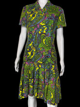 Load image into Gallery viewer, A short-sleeve collared dress with a vibrant green, yellow, purple, and blue paisley pattern, displayed on a white mannequin against a plain wall.