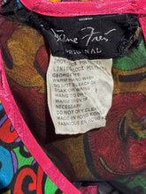 Load image into Gallery viewer, Close-up of the interior of a colorful garment or bag, showing a black fabric label with white script and a sewn-in care tag with product details. The surrounding fabric has a multicolor abstract print with bright pink trim.