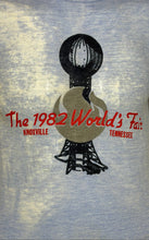 Load image into Gallery viewer, A close-up of a heather blue t-shirt featuring a graphic print of the 1982 World's Fair in Knoxville, Tennessee. The graphic includes a stylized fair building and red text reading 'The 1982 World's Fair' with 'KNOXVILLE' and 'TENNESSEE' below.