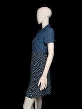 Load image into Gallery viewer, A short-sleeve denim dress displayed on a white mannequin, featuring a solid blue denim yoke and a blue-and-white floral patterned skirt.